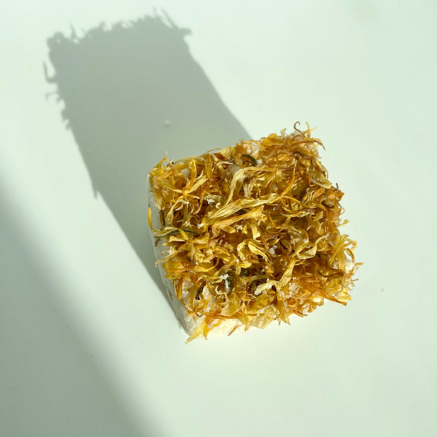 Marigold colored eucalyptus and peppermint bath bomb cube with dried calendula petals on top by Live Like You Green It pictured on a white background