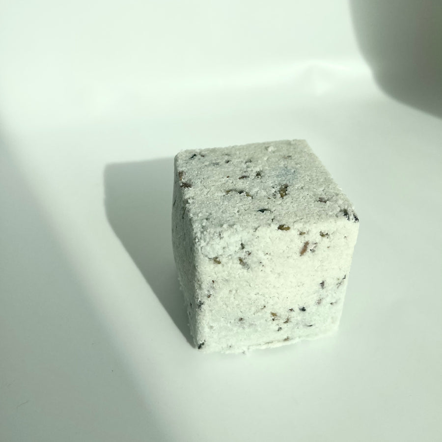 Lavender and blue tansy bath bomb cube with dried lavender petals mixed in by Live Like You Green It pictured on a white background